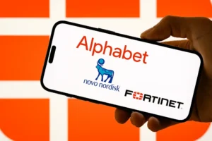 صورة لهاتف ذكي محمول باليد، تعرض شاشته شعارات ثلاث شركات كبرى: Alphabet، Novo Nordisk، وFortinet. تظهر الخلفية بألوان برتقالية لامعة مع نمط شبكي، مما يمنح المشهد طابعًا عصريًا يعكس قوة العلامات التجارية وتأثيرها في الأسواق العالمية.